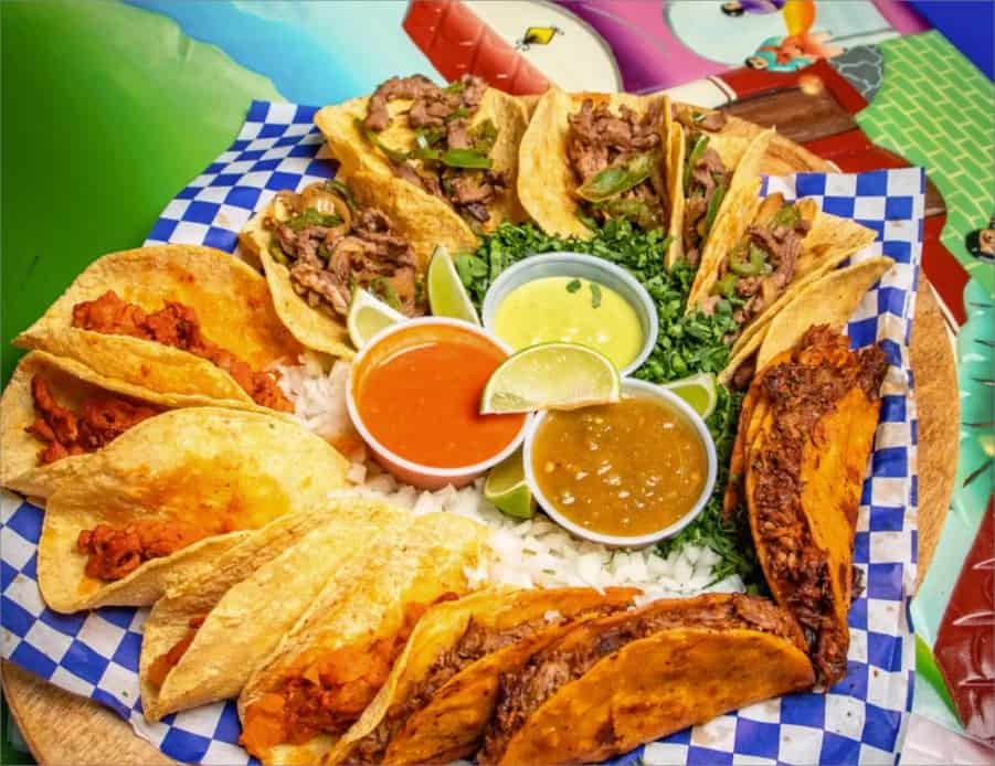 A vibrant platter of assorted tacos from a local taqueria, featuring various fillings and sauces on a colorful table.