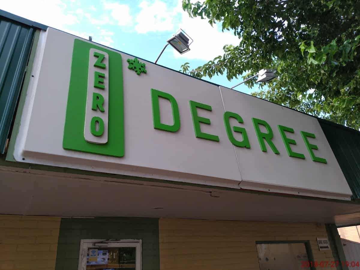 A sign reading "Zero Degree" in green letters on a white background is mounted on the facade of a green building, with tree branches overhead. It's a cool spot where you might just find your favorite bowl of pho waiting inside.
